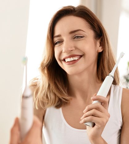 Woman with electric toothbrush looking in mirror and smiling