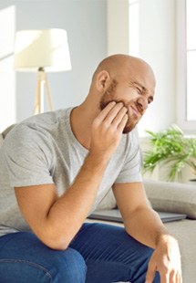 man with jaw pain sitting on couch 